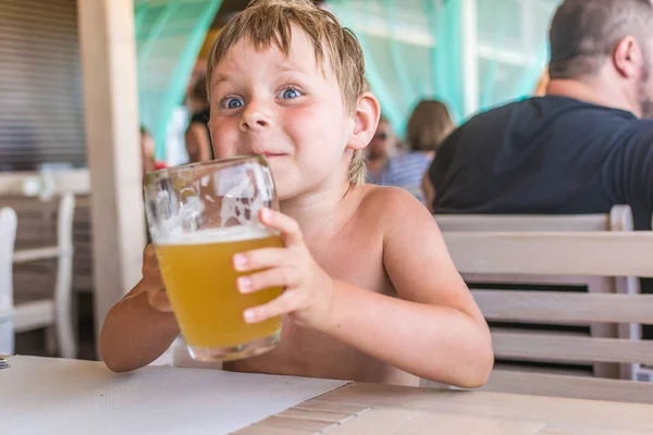 Маленький мальчик держит бокал пива на террасе летнего кафе . — стоковое фото