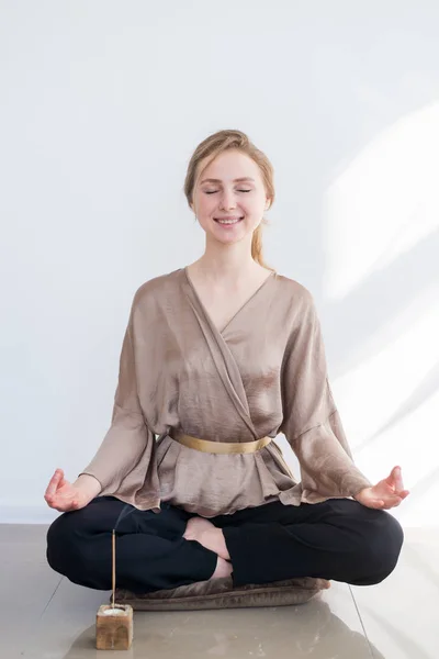 En ung attraktiv flicka mediterar när du sitter i en Lotus på golvet med en brännande arom. Meditation, hälsosamt liv, yoga koncept. — Stockfoto