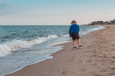 Küçük bir çocuk deniz kıyılarında, okyanus boyunca koşuyor. Yaz aylarında boş zaman aktiviteleri.