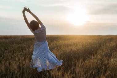Gün batımında bir buğday tarlası üzerinde bir elbise içinde orta yaş kadın. Özgürlük, doğalılık, doğa konsepti.