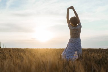 Gün batımında bir buğday tarlası üzerinde bir elbise içinde orta yaş kadın. Özgürlük, doğalılık, doğa konsepti.