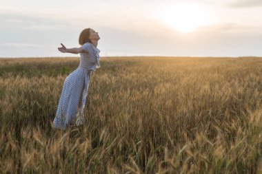 Gün batımında bir buğday tarlası üzerinde bir elbise içinde orta yaş kadın. Özgürlük, doğalılık, doğa konsepti.