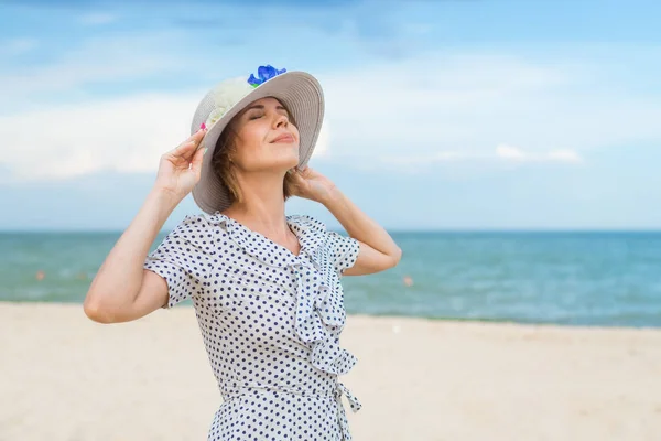 Middle age woman in hat and dress on the seashore, ocean. Leisure, vacation, serenity, freedom concept.