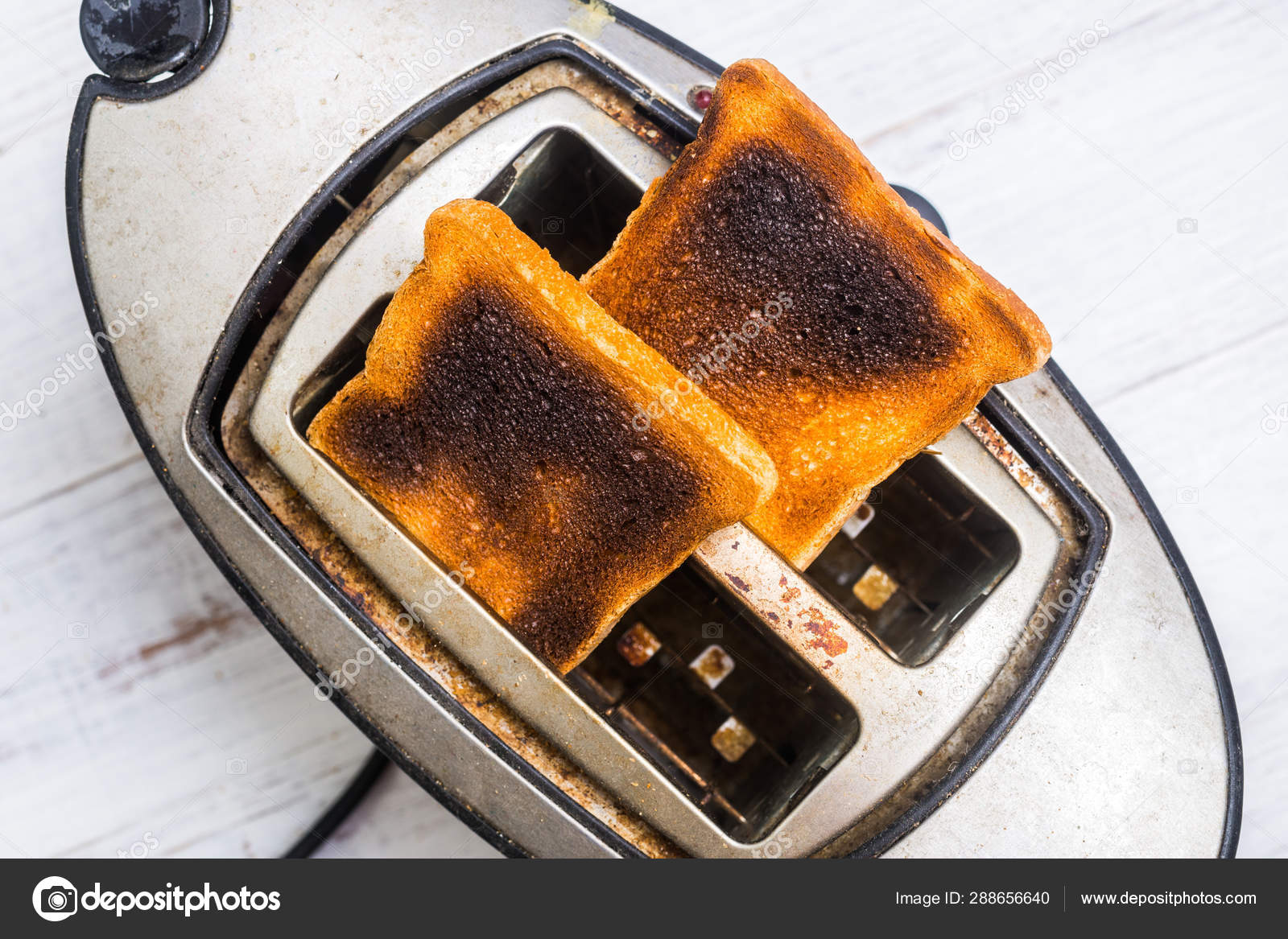 Dirty old toaster with burnt, overdone bread on a white wooden