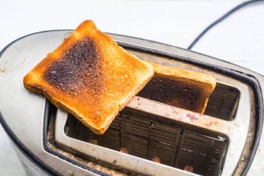 Beyaz ahşap arka planda yanmış, abartılı ekmek ile kirli eski tost makinesi. Kırık, arızalı mutfak aletleri.