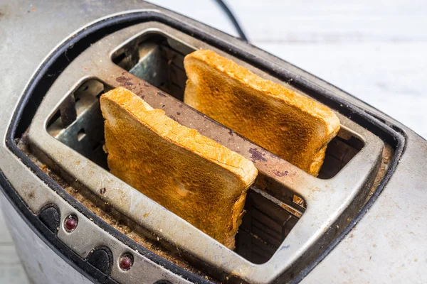 Dirty old toaster with bread on a white wooden background.