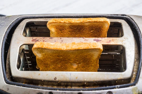 Torradeira velha suja com pão em um fundo de madeira branco . — Fotografia de Stock