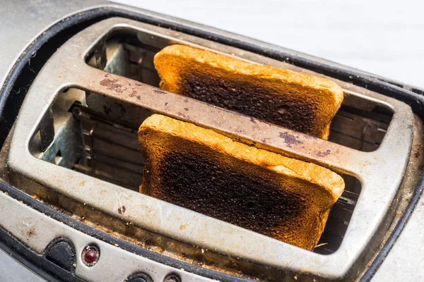 Dreckiger alter Toaster mit verbranntem, übertriebenem Brot auf weißem Holzgrund. Kaputte, defekte Küchengeräte. — Stockfoto