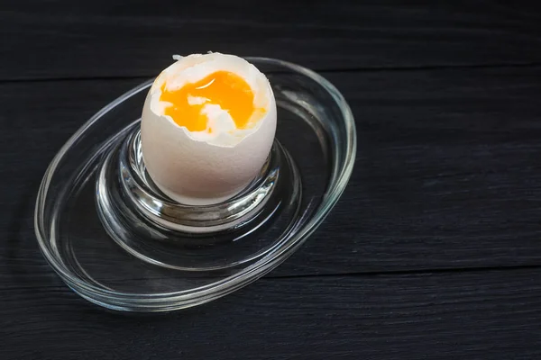 Boiled soft-boiled chicken egg on a black wooden background.