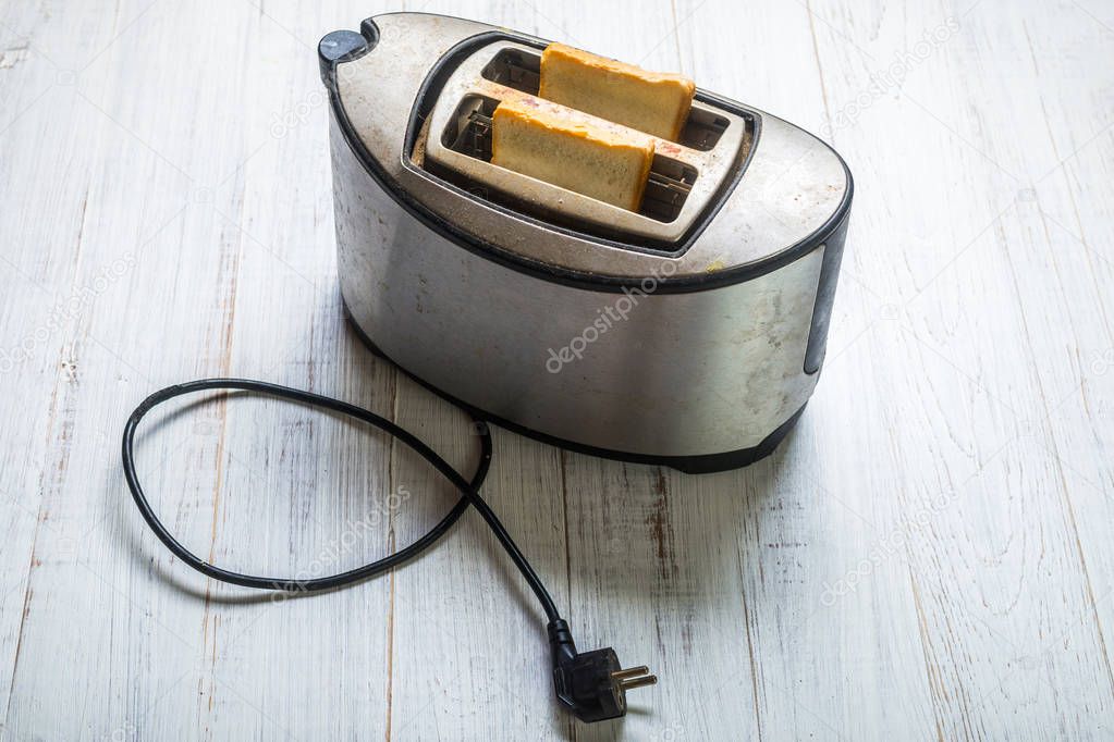 Dirty old toaster with bread on a white wooden background.