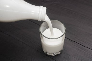 Siyah ahşap arka planda bir şişe bir bardak içine kefir dökme.