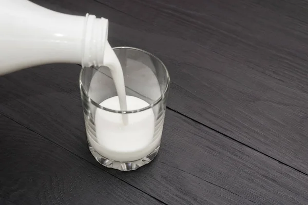 Het gieten van kefir in een glas uit een fles op een zwarte houten achtergrond. — Stockfoto