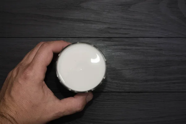 Mannelijke hand met een glas met kefir, yoghurt, melk op een zwarte houten achtergrond. — Stockfoto