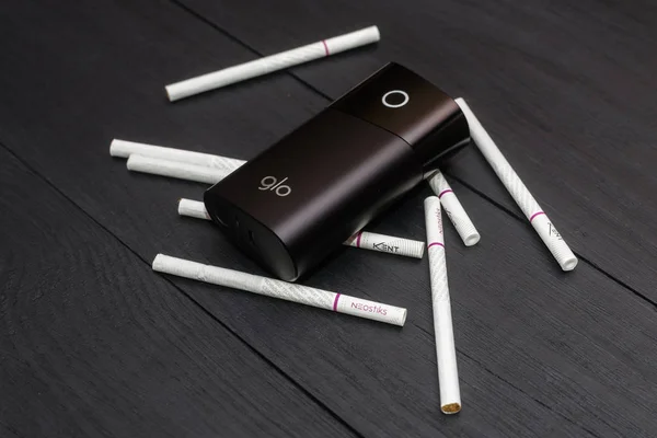 Kiev, Ukrayna-28 Temmuz 2019: GLO-siyah ahşap arka planda tütün ve sigara çubukları ısıtmak için bir cihaz.