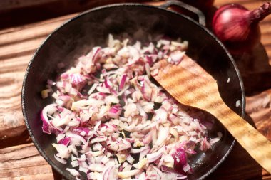 Bir tavada kızarmış kırmızı soğan ahşap spatula ile.