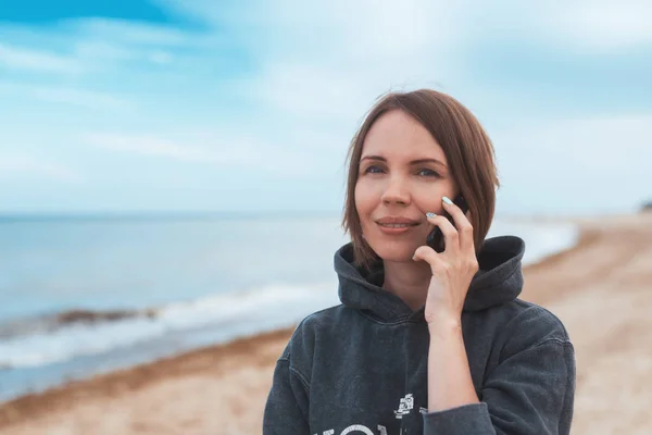 La femme sourit et communique par téléphone sur le bord de la mer, l'océan . — Photo