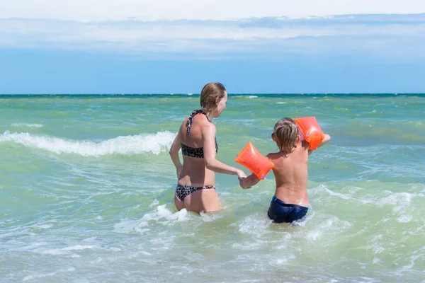 Мама с маленьким сыном плавает в морских волнах. Женщина и маленький мальчик брызгают в воду . — стоковое фото