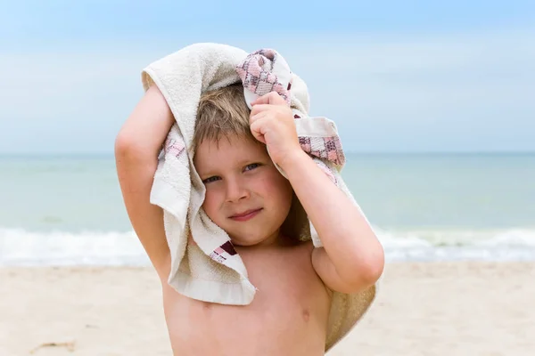 Malý chlapec si utírá mokrou hlavu s ručníkem na moři. — Stock fotografie