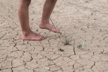 Kurumuş çatlak toprakta yürüyen bir çocuğun çıplak ayakları. Su eksikliği kavramı, susuzluk.