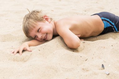 Yazın küçük bir çocuk kumda yatıyor. Çocuğun geri kalanı sahilde.