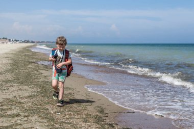 Küçük çocuk fotoğrafçı. Sırt çantası olan bir çocuk plajda fotoğraf yapar.