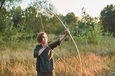 Bir kadın gün batımında doğada bir yay vuruyor.