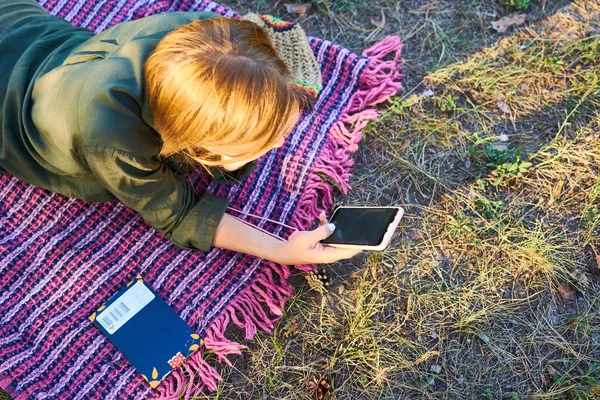 Žena středního věku leží na trávě s telefonem v dlaních. — Stock fotografie