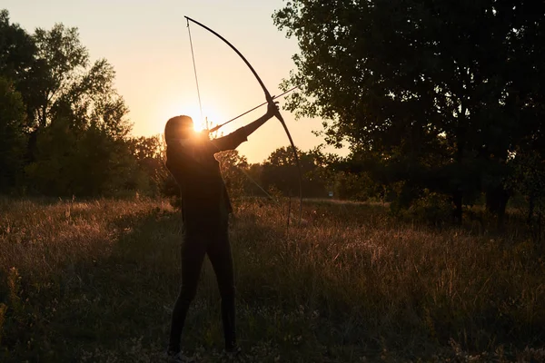 Una donna spara un arco nella natura al tramonto . — Foto Stock