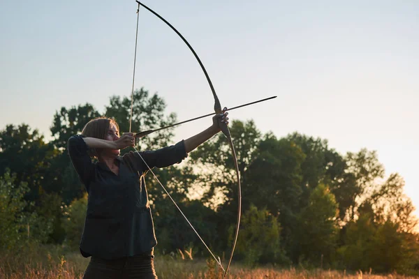 Una donna spara un arco nella natura al tramonto . — Foto Stock