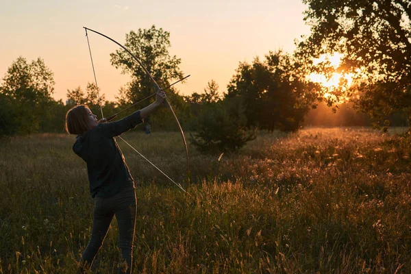 Una donna spara un arco nella natura al tramonto . — Foto Stock