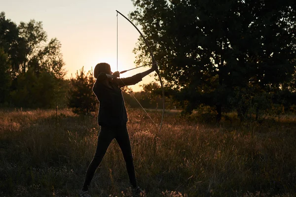 Una donna spara un arco nella natura al tramonto . — Foto Stock