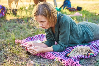 Orta yaşlı bir kadın ellerinde bir telefonla çimenlerin üzerinde yatıyor..