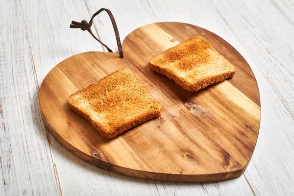 Toasted white bread toast on a wooden background in the shape of a heart.