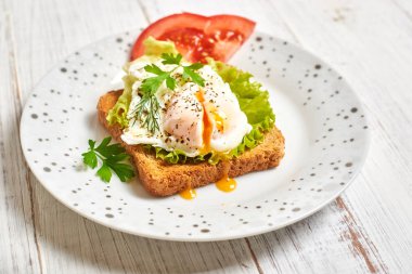Haşlanmış yumurta, kızarmış ekmek üzerine Benedict salata ve ahşap bir tabakta baharat..