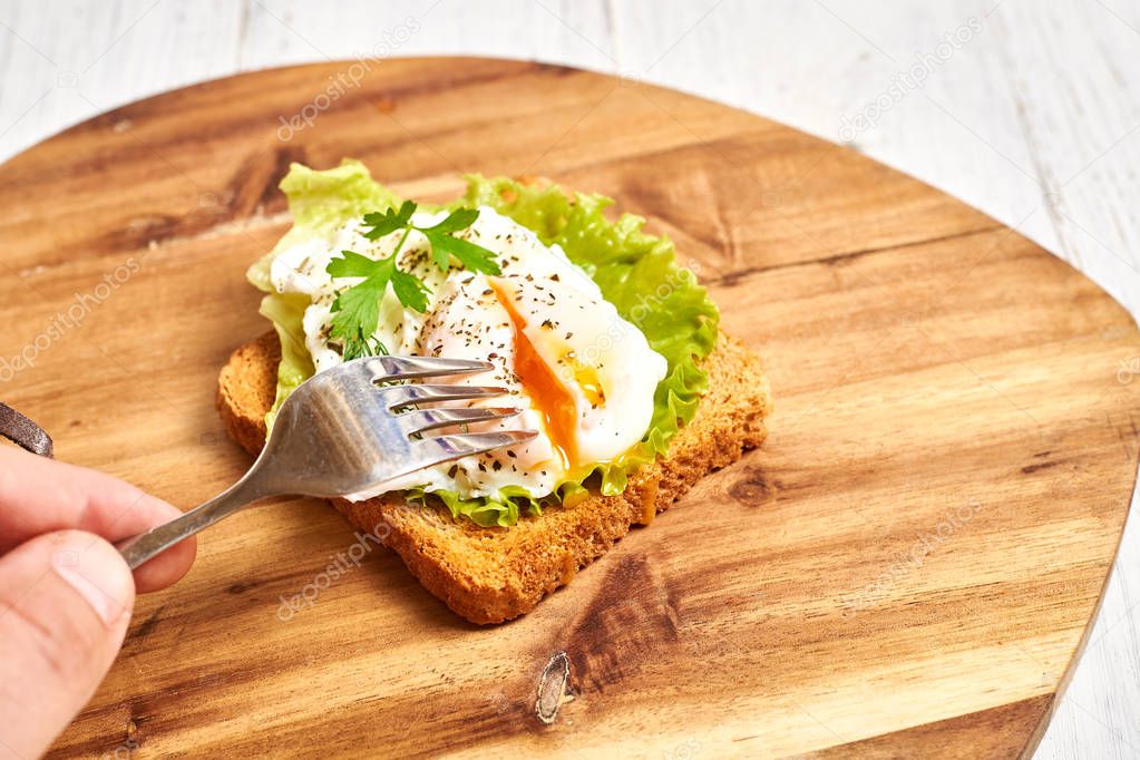 Poached egg, benedict on toasted white bread toast with salad and spices on a wooden background.