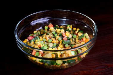 Donmuş farklı sebzeler, ahşap bir zeminde cam bir tabakta..