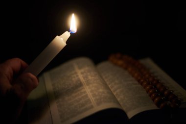 Erkek elinde yanan bir mum ve açık bir İncil, bir kitap. Tanrı 'ya, Hristiyanlığa, dine inanç kavramı.