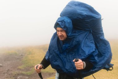 Kötü havada sislerin içinde yağmurluk içinde yürüyüş yapan bir adam..