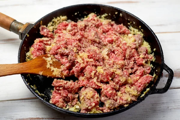 minced meat and onions in a pan on a light wooden background. Cooking toppings.