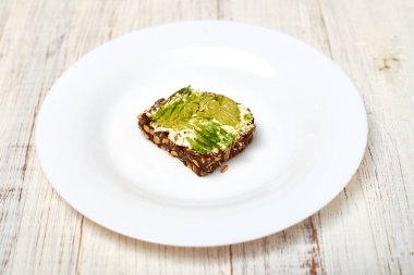 Mısır gevreği ekmeği, krem peynir ve beyaz tabakta avokado. Vejetaryen sandviçi.