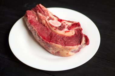 Siyah ahşap arka planda beyaz tabakta çiğ biftek..