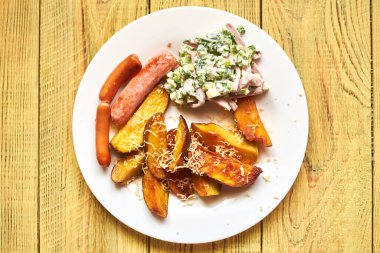 Kızarmış patates, peynirli, sosisli ve salatalı ahşap bir tabakta..