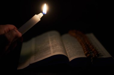 Erkek elinde yanan bir mum ve açık bir İncil, bir kitap. Tanrı 'ya, Hristiyanlığa, dine inanç kavramı.