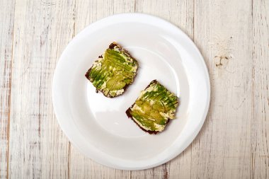 Mısır gevreği ekmeği, krem peynir ve beyaz tabakta avokado. Vejetaryen sandviçi.