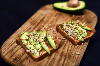 Dilimlenmiş avokadoyla tost, ahşap arka planda tohumların karışımı. Yarın sağlıklı atıştırmalıklar var. Düzgün beslenme, diyet kavramı.