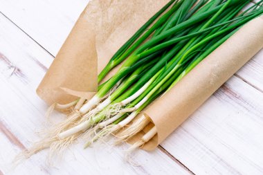 Hafif ahşap zemin üzerinde bir demet yeşil soğan.