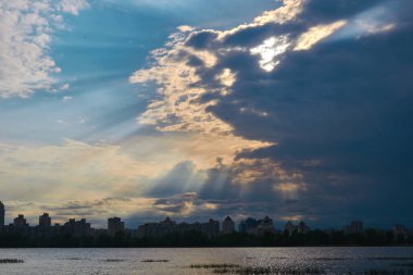 Nehrin ve şehrin üzerindeki kara bulutların arasından güneş ışınları süzülüyor..