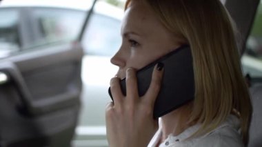 Sarışın bir kadın arabada cep telefonuyla konuşuyor..