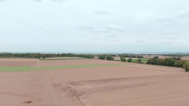 Tarım alanlarının geniş hava manzarası ve bulutlu gökyüzünün altındaki uzak kıyı şeridi.