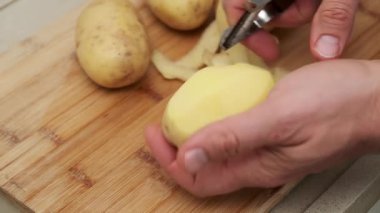 Ahşap kesim tahtasındaki taze patatesleri soyan ellerin yakın çekimi..